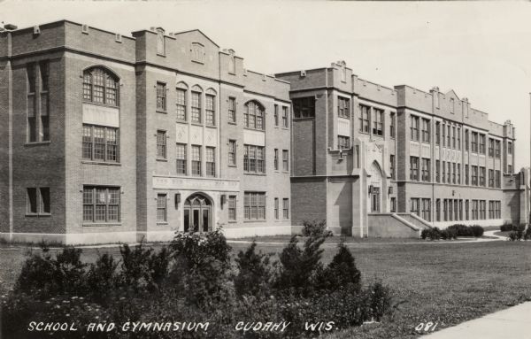 Photographic postcard view of brick school and gymnasium buildings. Caption reads: "School and Gymnasium, Cudahy, Wis."