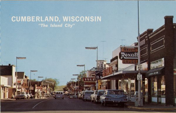 View down street of commercial buildings. Text on back reads: "A friendly city of prosperous, industrious people in a farming and vacationers' paradise. 'The Island City' is surrounded by the waters of Beaver Dam Lake and by a vacation and recreation area that includes some fifty lakes within a radius of 10 miles."