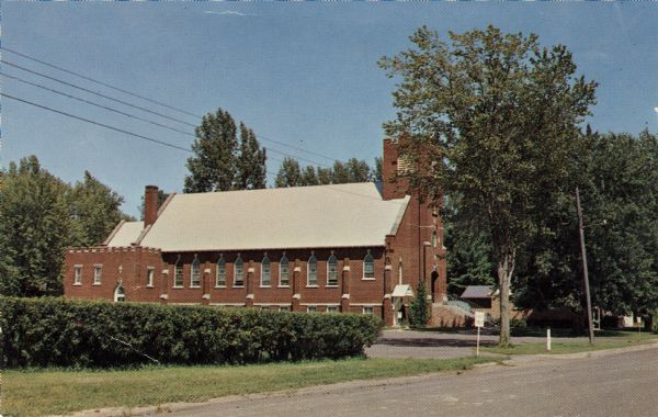 View from street of the brick church building. Printed on back: "St. Anthony Abbot Church, Cumberland, Wisconsin, Located South Edge of Town, Masses 7:30 AM and 10:30 AM."