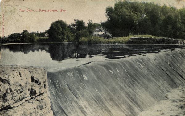 View across top of the Pecatonica River dam towards the opposite shoreline. Caption reads: "The Dam at Darlington, Wis."