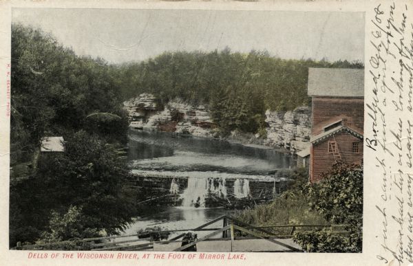 Photographic postcard of elevated view of the Dells of the Wisconsin River, at the foot of Mirror Lake. There is a bridge in the foreground, and a building at the right. Dated October 6, 1908. Caption reads: "Dells of the Wisconsin River, at the Foot of Mirror Lake."