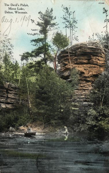 View across water towards a rock formation, "The Devil's Pulpit", on the shore of Mirror Lake. There is a man in a rowboat near the formation. Caption reads: "The Devil's Pulpit, Mirror Lake, Delton, Wisconsin."