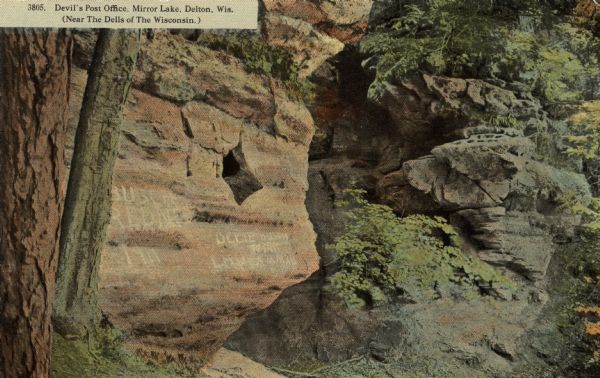 The Devil's Post Office rock formation, with a hole in the rocks, and graffiti. Near the Dells of the Wisconsin. Caption reads: "Devil's Post Office, Mirror Lake, Delton, Wis. (Near The Dells of The Wisconsin.)"