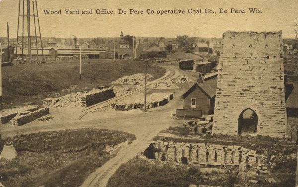 Elevated view of the wood yard and office. The stone structure on the right is the remnant of the National Furnace Company, an iron ore smelting company. Caption reads: "Wood Yard and Office, De Pere Co-operative Coal Co., De Pere, Wis."