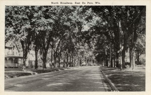 View down center of tree-lined residential street, with trees, sidewalks, lawns and houses on both sides. Caption reads: "North Broadway, East De Pere, Wis."