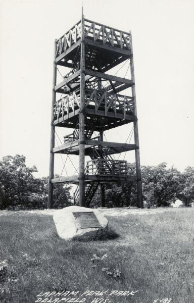 Black and white photographic postcard of the observation tower. In the foreground is a historic plaque embedded in a rock. Caption reads: "Lapham Peak Park, Delafield, Wis."