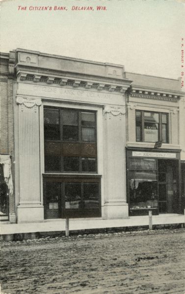 Photographic view from unpaved street of the facade of Citizens' Bank. A confectionery and a dentist's office are next door on the right. Caption reads: "The Citizen's Bank, Delavan, Wis."