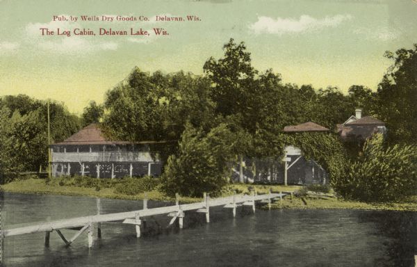 View from Delavan Lake of the "Log Cabin" resort on the shoreline. A long pier stretches from the shoreline off to the left. Caption reads: "The Log Cabin, Delavan Lake, Wis."
