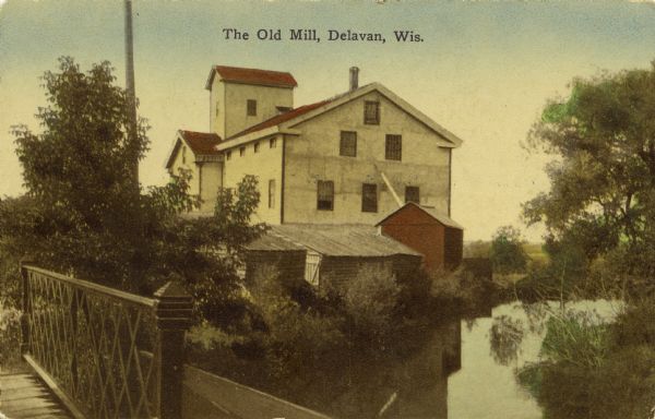 Hand-colored view of a mill as seen from a foot bridge. Caption reads: "The Old Mill, Delavan, Wis."