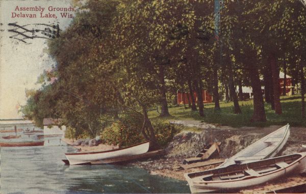 Hand-colored view towards shoreline of the Assembly Grounds along Delavan Lake. Row boats and canoes are pulled up on the shoreline. Caption reads: "Assembly Grounds, Delavan Lake, Wis."