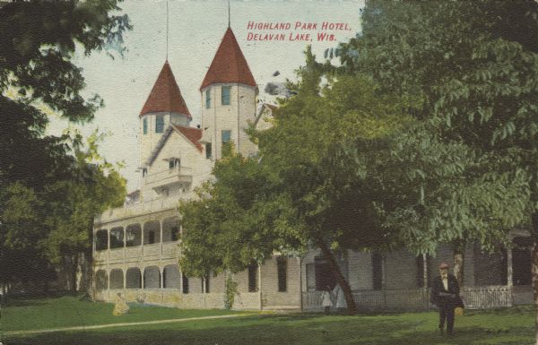 View across lawn towards the Highland Park Hotel, a large white building with twin spires and a wrap around porch and balcony. A number of people are standing on the lawn. Caption reads: "Highland Park Hotel, Delavan Lake, Wis."
