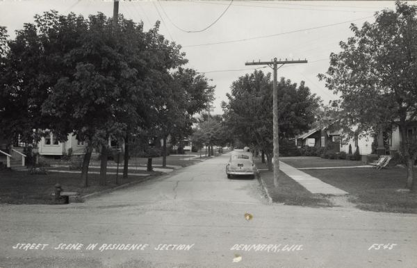 View from intersection of a residential street scene, with an automobile parked along the curb. Caption reads: "Street Scene in Residence Section, Denmark, Wis."