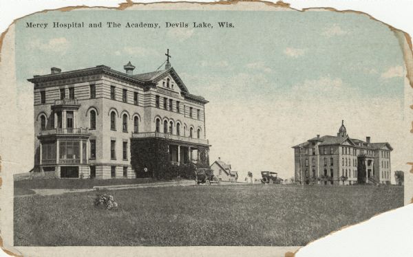 Color enhanced photographic postcard of Mercy Hospital and The Academy at Devils Lake, North Dakota with automobiles parked in front; incorrectly labeled as Devil's Lake, Wisconsin. 