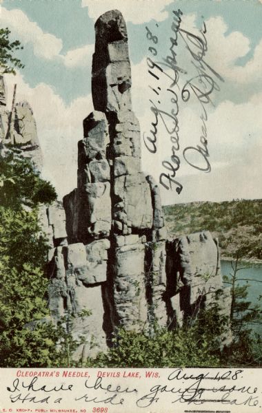 Colorized postcard view of the Cleopatra's Needle rock formation, with  Devil's Lake in the background. Caption reads: "Cleopatra's Needle, Devils [sic] Lake, Wis."