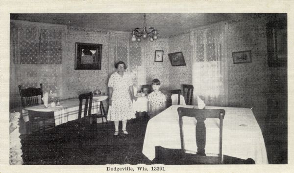 Woman and child standing in a room with three tables covered in tablecloths. Caption reads: "Dodgeville, Wis."