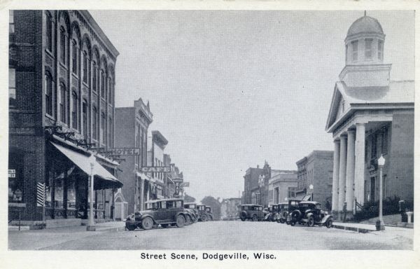 Iowa Street, looking south, with the Iowa County Courthouse on the right. Automobiles are parked at an angle on both sides of the street. Caption reads: "Street Scene, Dodgeville, Wisc."