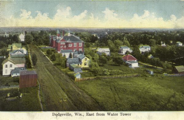 Elevated view of Dodgeville, with fields, houses, and lawns in the foreground, larger, brick buildings in the center, and a church in the distance. Caption reads: "Dodgeville, Wis., East from Water Tower."