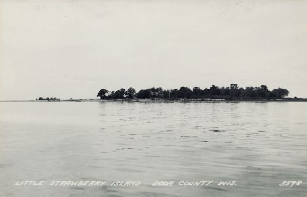 View across water towards Little Strawberry Island in Green Bay. The beach on the left side of the island is sandy, and a house can be seen among the trees.
