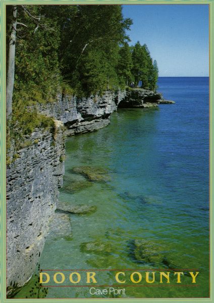 View from top of cliff looking at Cave Point along the shoreline of Lake Michigan. The text on the reverse reads: "Cave Point. This popular tourist spot is located on the peninsula's Lake Michigan side in Cave Point County Park. Waves breaking against undercut limestone cliffs cause a 'booming' sound that can be heard a quarter-mile away."
