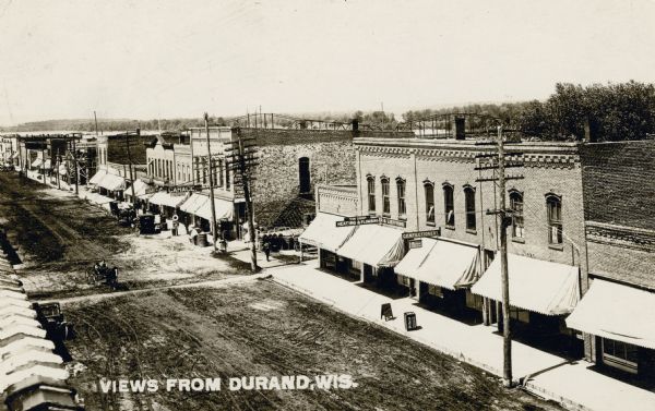 Elevated view towards one side of Main Street, with the bridge over the Chippewa River in the background. Commercial buildings are along the sidewalk, and there are horse-drawn vehicles and telephone lines along the curb. Caption reads: "Views from Durand, Wis."