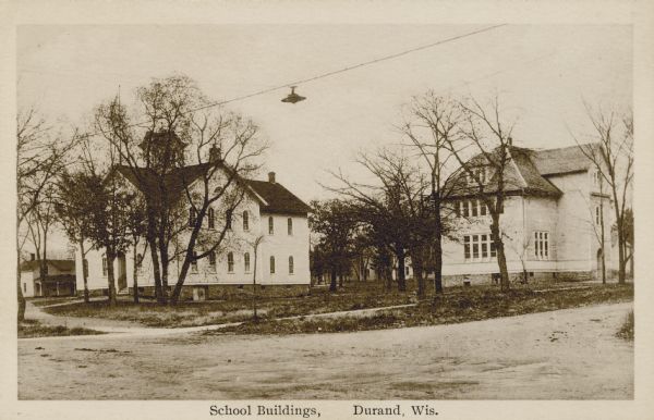 View from street towards two white frame school buildings. Old high school building, 1876-1923. Caption reads: "School Buildings, Durand, Wis."