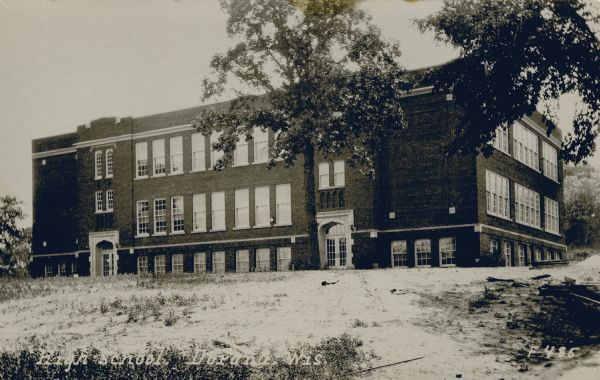 View looking up slope towards the brick high school building. Snow is on the ground. Caption reads: "High School, Durand, Wis."