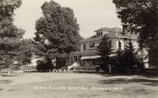 Black and white photographic postcard view of a large white building with awnings, labeled as the Pepin County Hospital. Caption reads: "Pepin County Hospital, Durand, Wis."