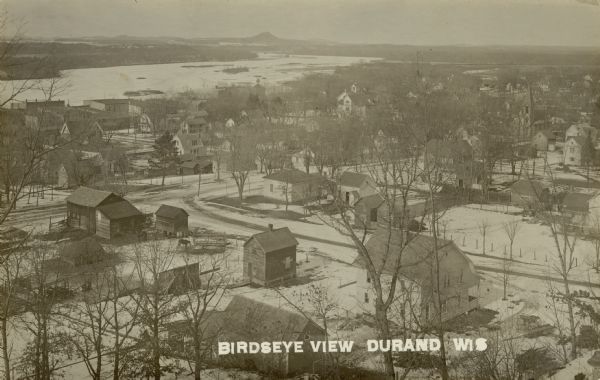 Elevated view of the town with snow on the ground. Houses are near an intersection in the foreground, and homes and commercial buildings are along the shoreline of the Chippewa River in the background. Caption reads: "Birdseye [sic] View, Durand, Wis."