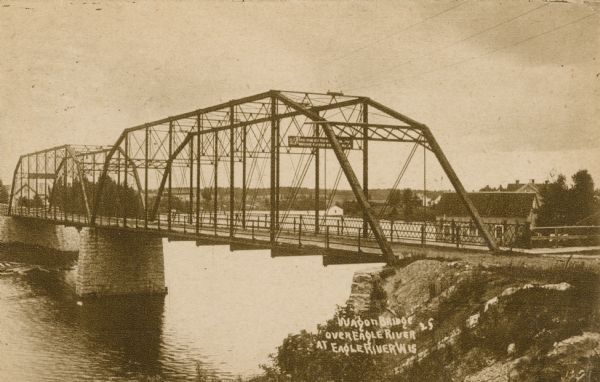 View from shoreline of the Wagon Bridge, which has a steel frame and stone piers. Possibly on Railroad Street. Caption reads: "Wagon Bridge over Eagle River, Eagle River, Wis."
