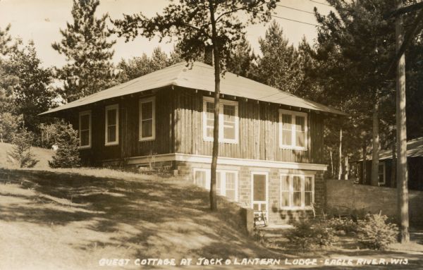 View of cottage built into a hill on Taylor Lake east of Eagle River on STH 70. Caption reads: "Guest Cottage at Jack O'Lantern Lodge — Eagle River, Wis."