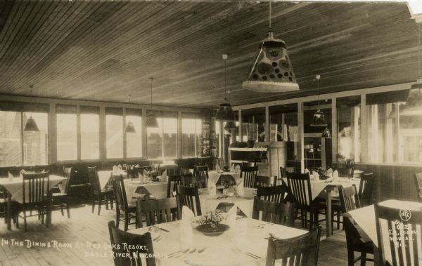 Dining Room at the Red Oaks Resort, with tables and chairs set for dining. The windows in the background look out at other buildings. Caption reads: "In The Dining Room at Red Oaks Resort, Eagle River, Wisconsin."
