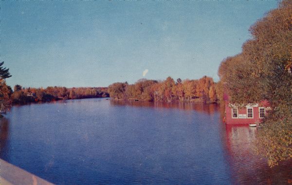 Elevated view of fall color on Yellow Birch Lake on the Eagle Chain of Lakes. There is a boathouse on shoreline at the right obscured by trees.
