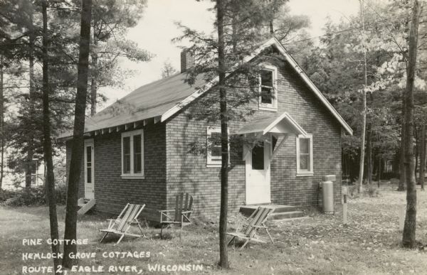 Cottage at the resort with chairs on the grass in front. Caption reads: "Pine Cottage, Hemlock Grove Cottages, Route 2, Eagle River, Wisconsin."