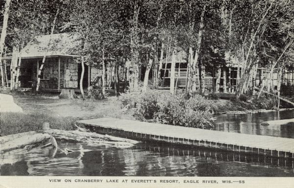 View across water towards lakeside cabins among birch trees at the resort on Catfish Lake, east of Eagle River off of STH 70. There is a pier in the foreground. Caption reads: "View on Cranberry Lake at Everett's Resort, Eagle River, Wis."
