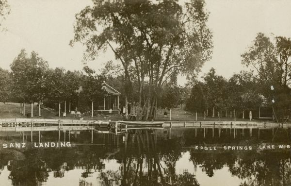 Black and white photographic postcard view across water towards Sanz Landing. Caption reads: "Sanz Landing, Eagle Springs Lake, Wis."