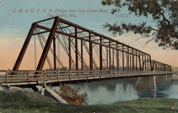 Hand-colored view of a railroad bridge with two men standing on it. There are buildings in the background on the far shoreline. Caption reads: "C.M. & St. Paul R.R. Bridge over Eau Claire River, Eau Claire, Wis."