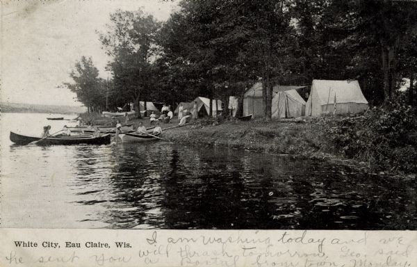 View along shoreline towards a campsite on the shores of the Chippewa River. People are in rowboats on the river. Caption reads: "White City, Eau Claire, Wis."