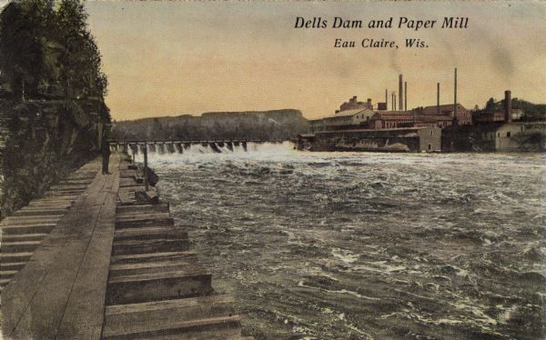 View of the dam at the Dells of the Chippewa River. The paper mill is in the background on the opposite shoreline. Caption reads: "Dells Dam and Paper Mill, Eau Claire, Wis."