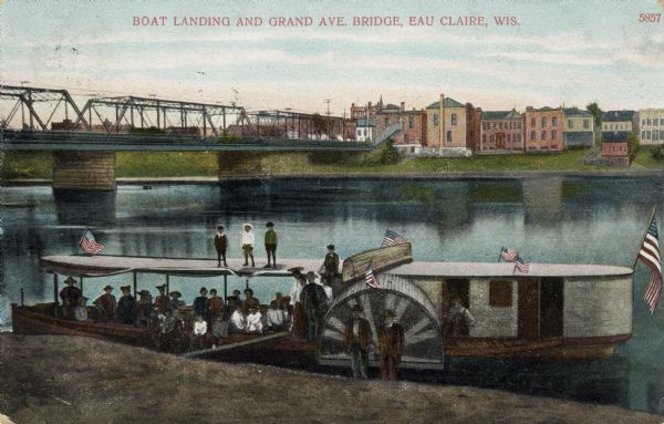 Colorized photograph of the Chippewa River, with the Grand Avenue Bridge on the left. In the foreground at the shoreline is a group of people at a boat landing with an excursion boat. Caption reads: "Boat Landing and Grand Ave. Bridge, Eau Claire, Wis."
