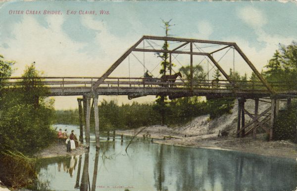 A colored photographic view from shoreline towards a truss bridge over the Otter Creek bridge. A horse and buggy are traveling on the bridge, and a woman and three children are fishing at the shoreline under the bridge. Caption reads: "Otter Creek Bridge, Eau Claire, Wis."