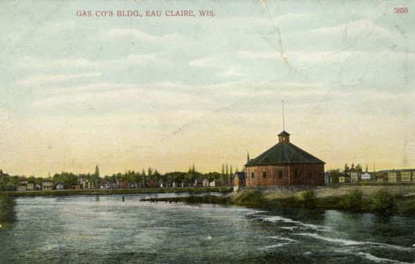Colorized photographic postcard of the Gas Company's building along the river in Eau Claire. Caption reads: "Gas Co's Building, Eau Claire, Wis."