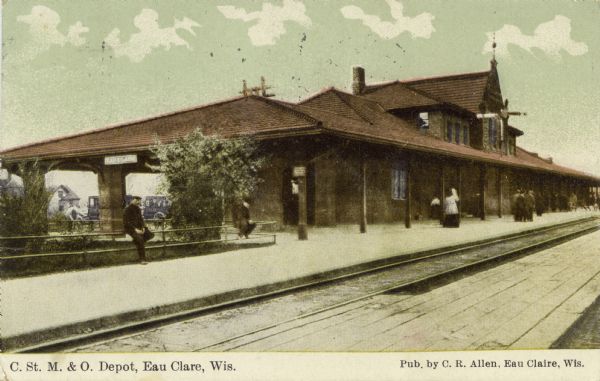 Color enhanced photograph of the depot for the Chicago, St. Paul, Minneapolis, & Omaha Railroad. There are horse-drawn carriages and pedestrians at the depot. Caption reads: "C. St. M. & O. Depot, Eau Claire, Wis."