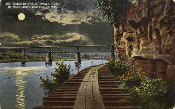 View of the dells on the Chippewa river. The night view shows a wooden walkway along the base of the cliff leading toward a railroad bridge across the river, with a full moon in the sky. Caption reads: "Dells of the Chippewa River. By Moonlight, Eau Claire, Wis."