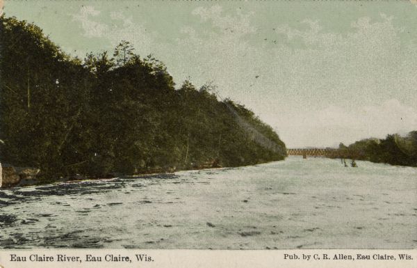 Color photograph of the Eau Claire river, with a railroad bridge in the distance. Caption reads: "Eau Claire River, Eau Claire, Wis."
