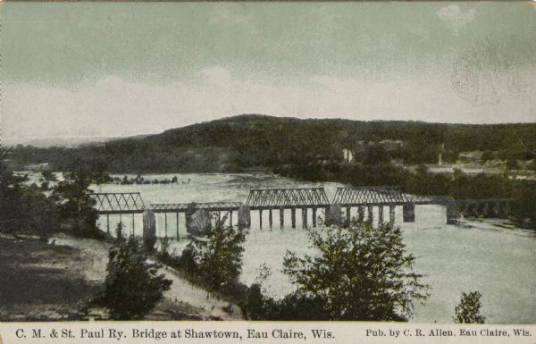 Color enhanced photographic view of the Chicago, Milwaukee, and St. Paul steel truss railroad bridge over the Chippewa River at Shawtown, near Half Moon Lake. The Daniel Shaw & Co. lumber company founded Shawtown, which was annexed to the City of Eau Claire by the 1930s. Caption reads: "C.M. & St. Paul Ry. Bridge at Shawtown, Eau Claire, Wis."