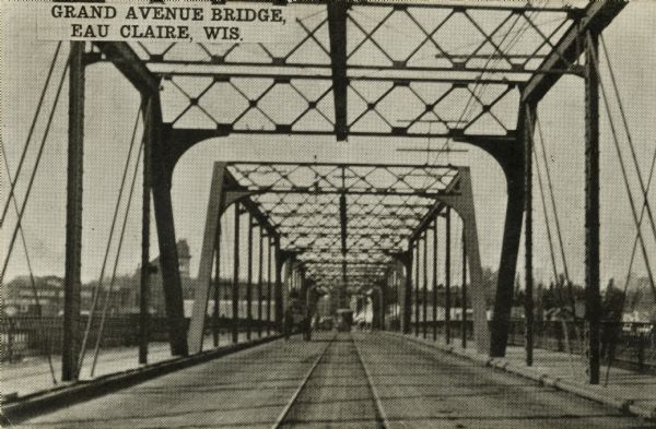 Black and white photographic postcard view of the Grand Avenue bridge across the Chippewa river, looking through the trusses along the streetcar tracks. Caption reads: "Grand Avenue Bridge, Eau Claire, Wis."