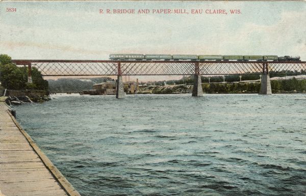 Enhanced photographic postcard of a lattice deck truss railroad high bridge and paper mill on the Chippewa River. The bridge was built in 1880 by the Chicago, St. Paul Milwaukee and Omaha Railroad. Caption reads: "R.R. Bridge and Paper Mill, Eau Claire, Wis."
