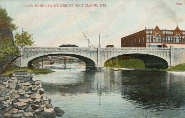 Color enhanced photographic postcard view of the "new" Barstow Street concrete arch bridge over the Eau Claire River. A street car is crossing the bridge. Caption reads: "New Barstow St. Bridge, Eau Claire, Wis."
