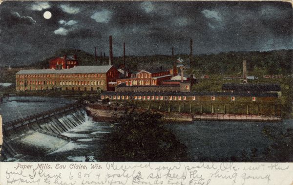 Colorized view of the paper mills on the Eau Claire River at night, with the moon in the cloudy sky in the background. There is a dam on the river in the foreground. Caption reads: "Paper Mills, Eau Claire, Wis."