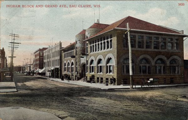 View across intersection towards the corner of Ingram and Grand Avenue. A large stone building with arched windows is in the foreground. Caption reads: "Ingram Block and Grand Ave., Eau Claire, Wis."